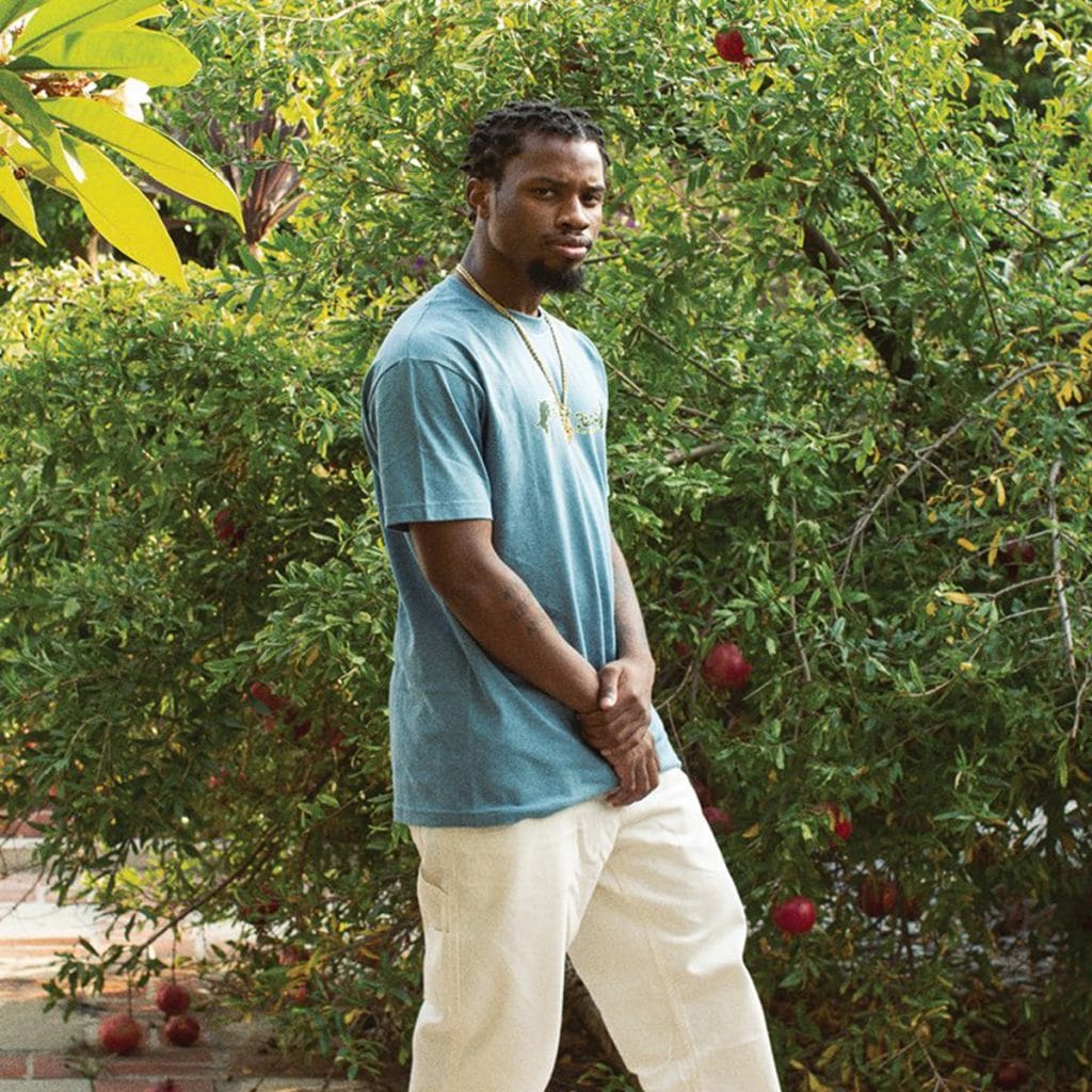 rapper denzel curry poses in front of shrubbery