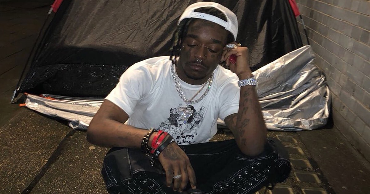 rapper lil uzi vert sits on sidewalk in front of tent