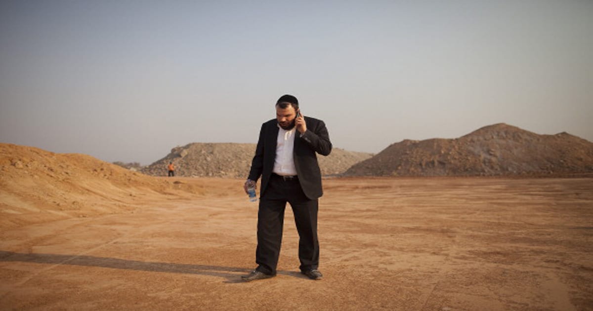 Dan Gertler talks on his smartphone while walking past mining rubble