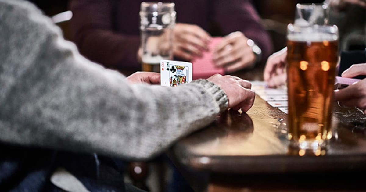 The men are playing cards in a traditional British pub, the image shows the hand of of the players which is in focus